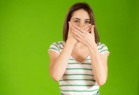 Portrait of beautiful and young woman standing over isolated green background asking to be quiet...