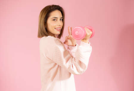 Beautiful young woman holding dumbbell isolated over pink background.