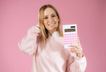 Young smiling woman with calculator on pink backgroundの写真素材
