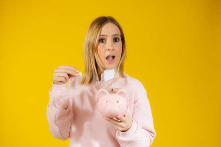 young caucasian pretty woman against yellow wall with a piggy bank