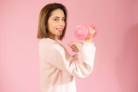 Beautiful young woman holding dumbbell isolated over pink background.の写真素材