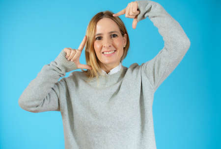 Young beautiful caucasian woman wearing casual shirt standing over isolated blue background smiling making frame with hands and fingers with happy face. Creativity and photography concept.の写真素材