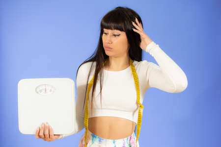 Surprised woman holding a measuring tape as dieting symbol and weight scales