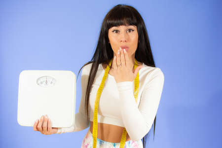 Surprised woman holding a measuring tape as dieting symbol and weight scalesの写真素材