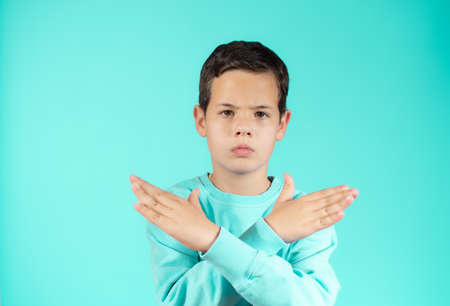 Cute Caucasian kid boy wearing casual sweater against green wall. Angry expression on face and crossing hands doing refusal negative sign.の写真素材