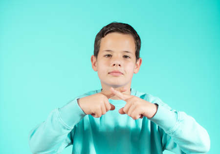 Cute Caucasian kid boy wearing casual sweater against green wall. Angry expression on face and crossing hands doing refusal negative sign.の写真素材