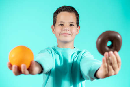 Young boy choosing between a orange and donuts isolated over green backgroundの写真素材