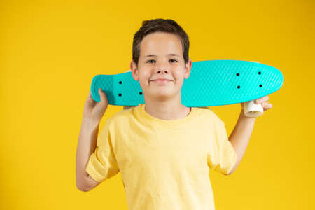 Full length portrait of an adorable young boy riding a skateboard isolated against yellow backgroundの写真素材