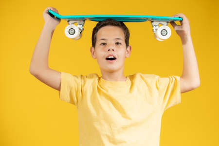 Full length portrait of an adorable young boy riding a skateboard isolated against yellow backgroundの写真素材