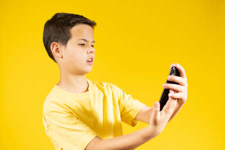 Young caucasian boy with phone isolated over yellow backgroundの写真素材