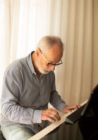 Man practicing playing the piano in the living room of his home after retirement from work.