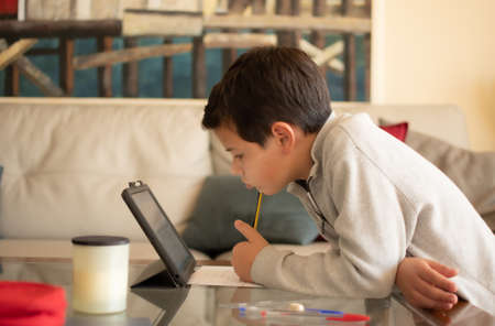 Portrait of a boy doing his homework at the laptop, isolated in the living roomの写真素材