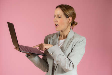 Surprised business woman holding laptop computer over pink backgroundの写真素材