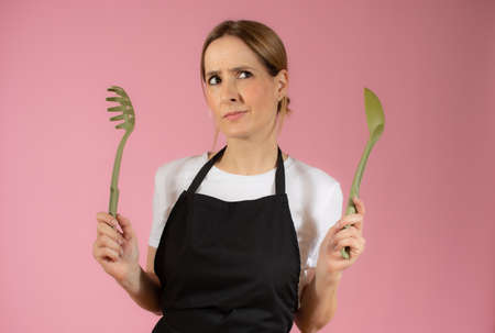 Young caucasian woman holding kitchen utensils against pink backgroundの写真素材