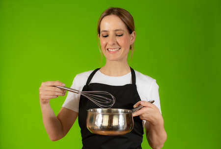 Young caucasian woman holding kitchen utensils against green backgroundの写真素材