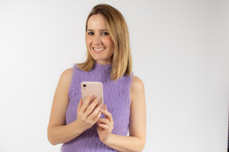 Portrait of a smiling young woman using mobile phone isolated over white backgroundの写真素材