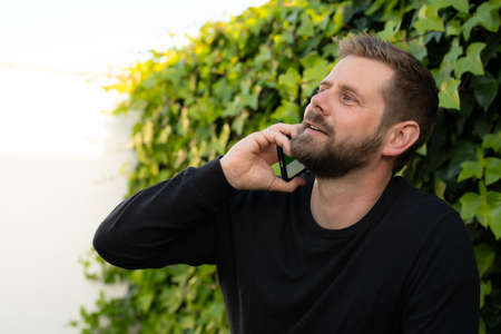 Young man sitting outdoors, talking on the phone.の写真素材