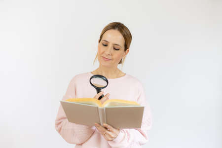 young woman holding a book looking through a magnifying glass