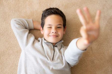 Top view of happy little boy lying on the floor with okay signの写真素材