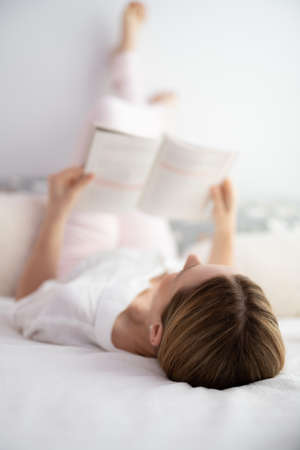Woman lying on the bed reading a bookの写真素材
