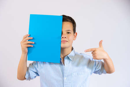 Cute boy holding blue blank paper covering eye isolated over white backgroundの写真素材