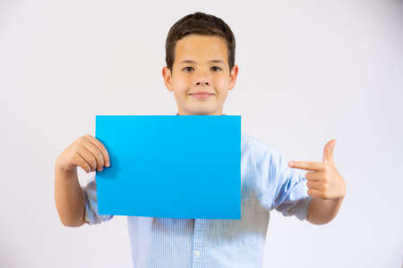 Cute boy pointing finger a blue blank paper isolated over white backgroundの写真素材