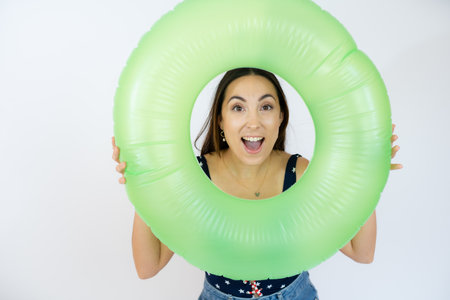 Young woman ready for swimming, wearing swimsuit and holding inflatable donuts ring, posing over white backgroundの写真素材