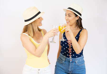 Two cheerful young women girls friends in summer clothes with straw hat, holding beverages isolated over white background.の写真素材