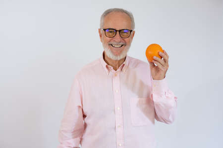 Portrait of cheerful senior man who is holding orange and smiling.の写真素材