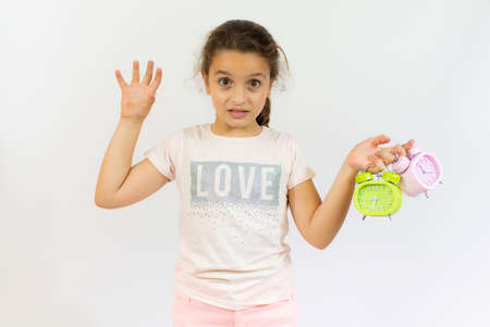 Portrait of little girl holding two alarm clocks isolated on white backgroundの写真素材