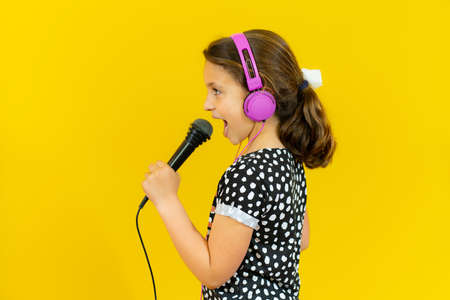 little pretty child listening music in headphones and singing isolated over yellow backgroundの写真素材