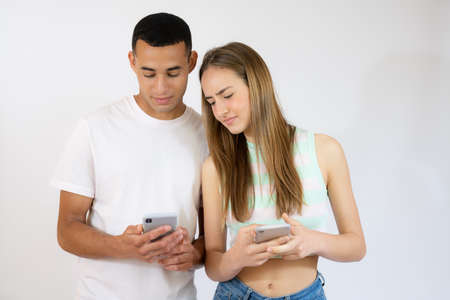 Young man and woman in casual wear standing and holding mobile phone isolated over white background