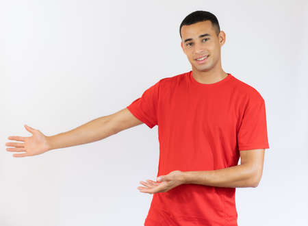 Young handsome man in casual t-shirt showing with hands product isolated over white background.の写真素材