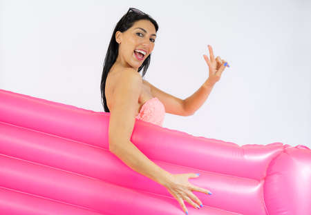 Beautiful young woman wearing swimsuit and holding summer float with victory signの写真素材