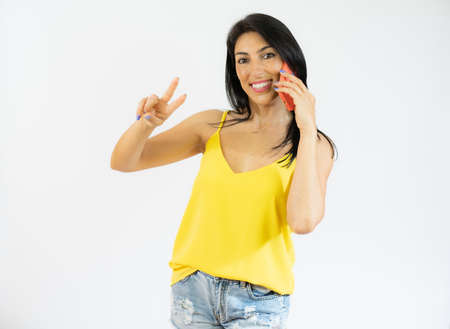 Portrait of happy woman talking on mobile phone with victory sign isolated over white background.の写真素材