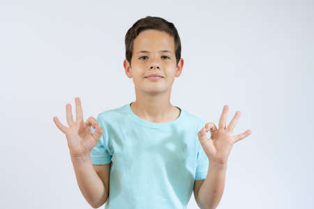 Let's hug. Portrait of friendly hospitable little boy in black T-shirt smiling happily and holding hands wide open to embrace, welcome. indoor studio shot isolated on blue backgroundの写真素材