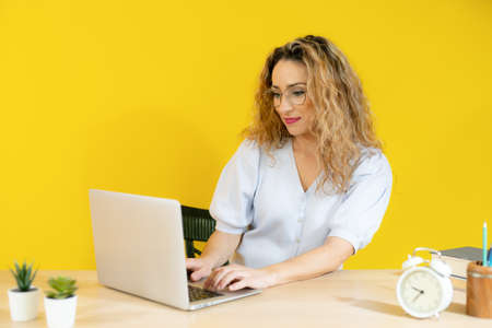 Young woman working on computer laptop concentrated and smiling over yellow background.の写真素材