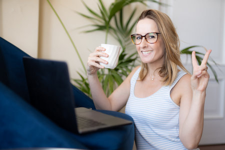 Attractive young woman working on laptop and drinking coffee while sitting on the floor at homeの写真素材