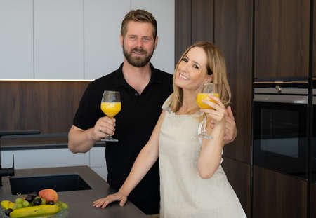 Beautiful couple standing on kitchen with fresh orange juice for breakfastの写真素材