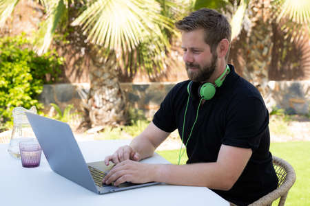 Side view handsome young businessman working with computer remotely, sitting at wooden table in terrace.の写真素材