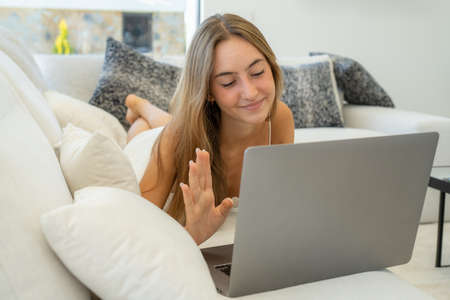 Pretty young woman using laptop sitting on sofaの写真素材
