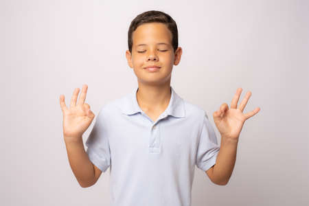 Portrait of peaceful cute little boy holding fingers in mudra gesture and meditating with closed eyes, feeling calm positive and relaxed, yoga practiceの写真素材