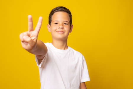 A happy shouting boy showing a victory sign isolated over yellow backgroundの写真素材