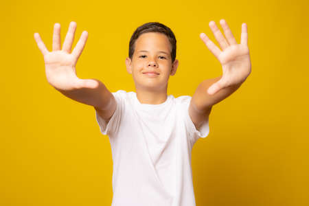 little cute Caucasian boy kid wearing white t-shirt against yellow wall doing stop gesture with palm of the handsの写真素材