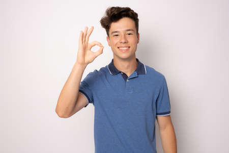 Happy young man in casual clothing with okay sign isolated over white background.の写真素材