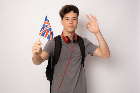 Cute student in casual clothes posing with british flag with okay sign isolated over white background.の写真素材