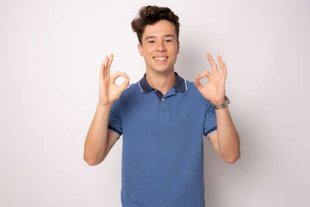 Happy young man in casual clothing with okay sign isolated over white background.の写真素材
