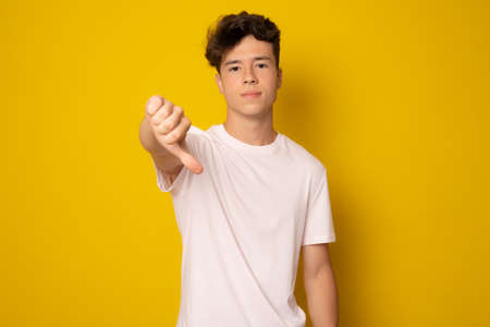 Young man wearing casual t-shirt standing over isolated yellow background looking unhappy and angry showing rejection and negative with thumb down gesture. Bad expression.の写真素材