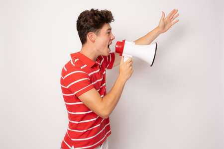 Handsome young man over isolated white background shouting through a megaphoneの写真素材