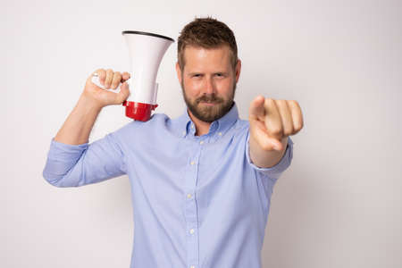 Young man holding a megaphone with serious face and pointing finger to camera isolated over white background.の写真素材
